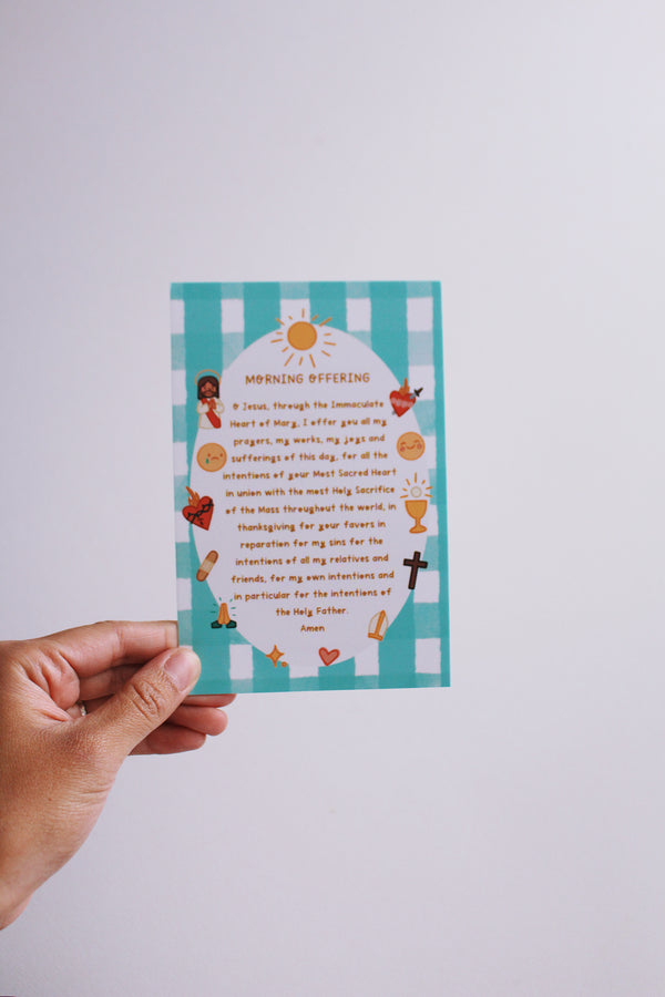 Hand holding a colorful prayer card with text and illustrations on a light gray background