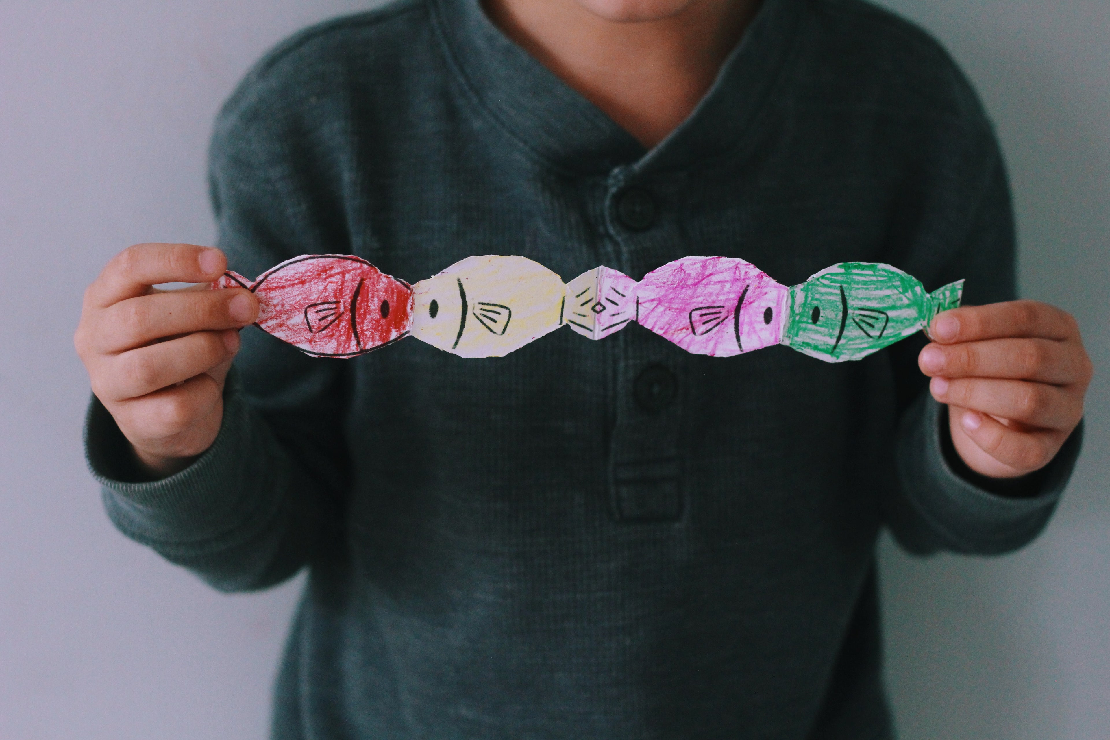 Person holding a colorful paper chain of fish shapes against a plain background