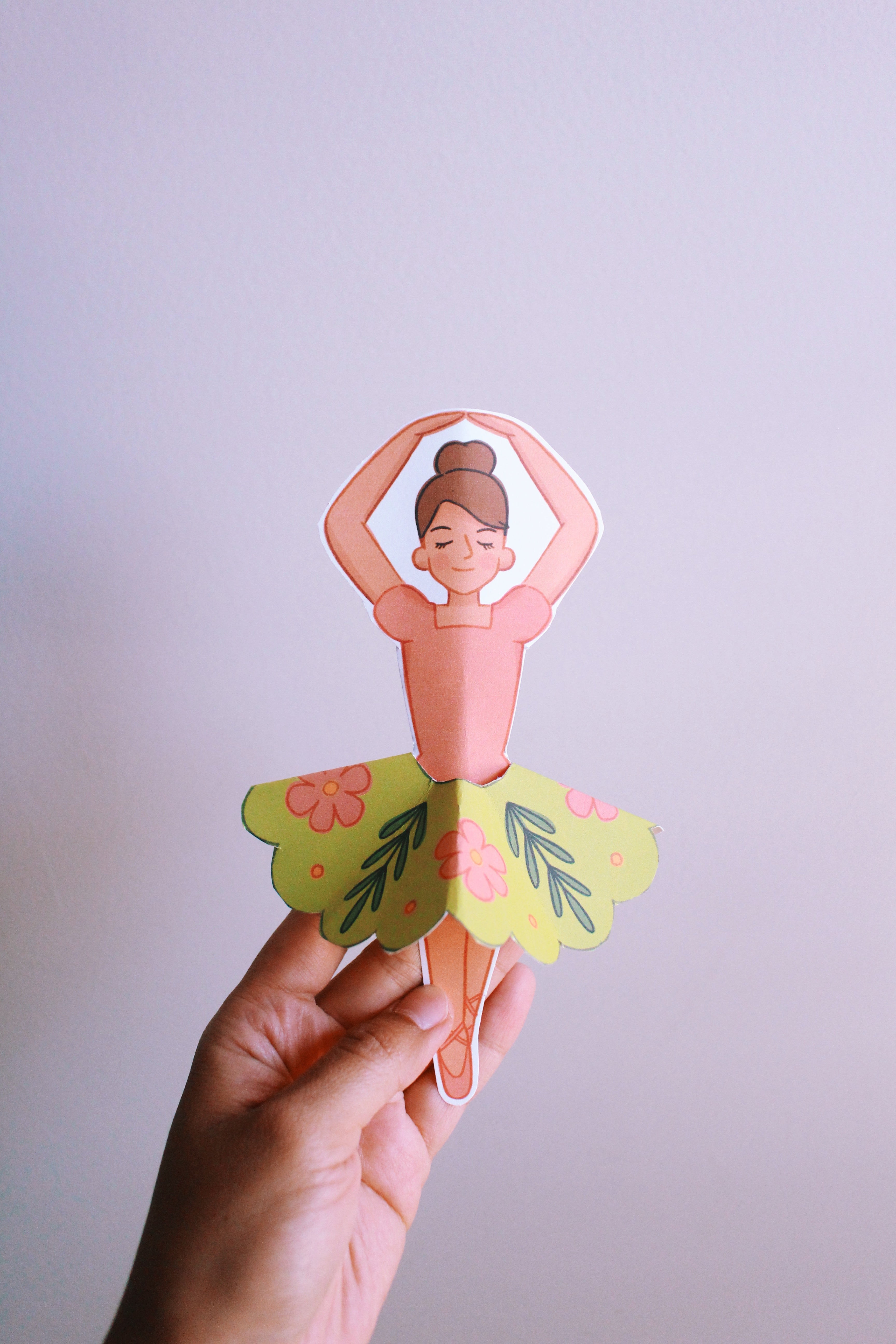 Hand holding a paper cutout of a woman with floral elements against a plain background