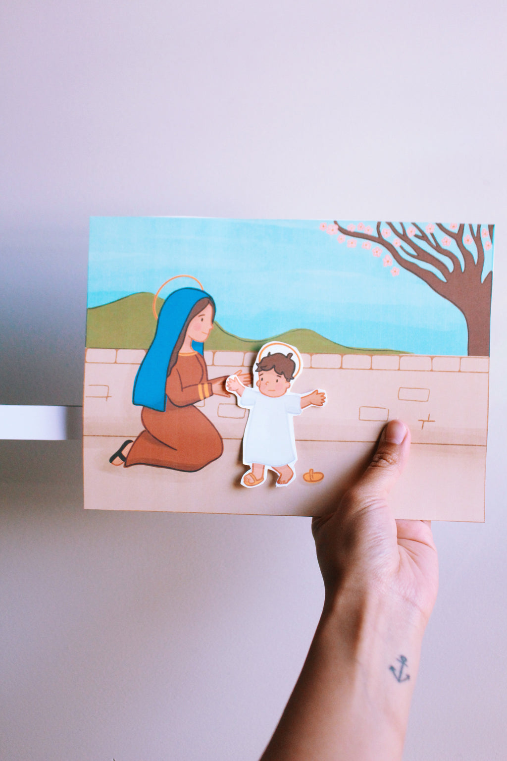 Hand holding a paper cutout of a woman and child against a scenic background