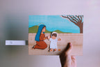Hand holding a paper cutout of a woman and child against a plain background