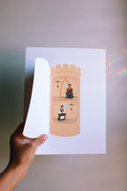 Hand holding a paper cutout of a castle with saint thomas more and john fisher inside against a plain background