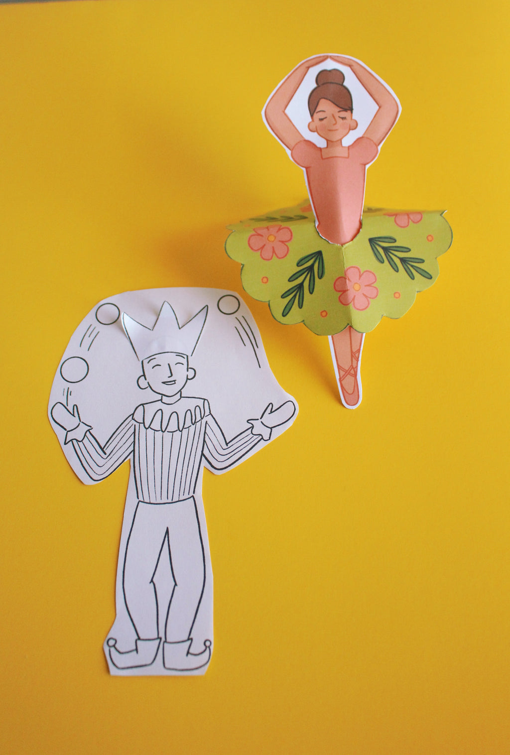 Two paper cutouts of a clown and a ballerina on a yellow background